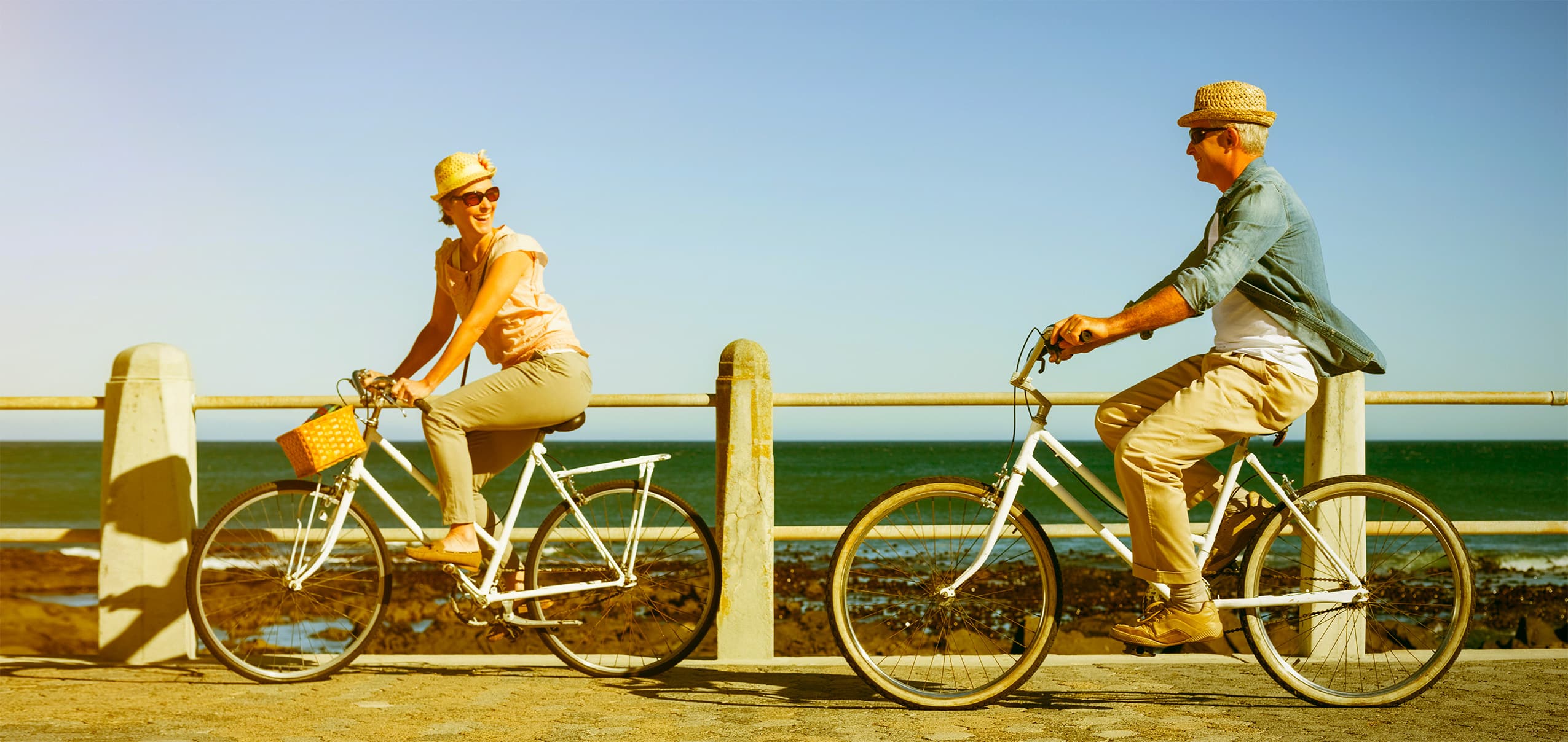 full-length-happy-couple-riding-bicycles-pier-against-sea